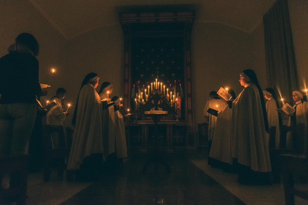 Nuns praying by candlelight, embracing the presence of God with each other. 